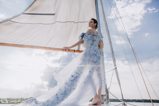 ?oung girl stands on a yacht with white sails in a flying dress.