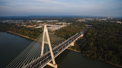 Aerial flight above the Megyeri bridge in Budapest Hungary. Cars cross the bridge. A boat drives under the bridge on the Danube.
