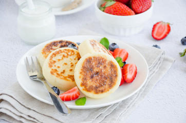 Fried cottage cheese pancakes or syrniki with fresh berries on a white plate with sour cream. Gluten free. Traditional breakfast of Ukrainian and Russian cuisine. Horizontal, close up