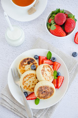 Fried cottage cheese pancakes or syrniki with fresh berries on a white plate with sour cream. Gluten free. Traditional breakfast of Ukrainian and Russian cuisine. Vertical, top view.