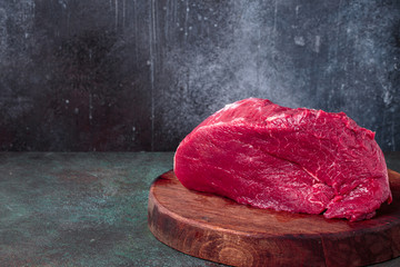 Raw beef on chopping deck on rust background with copy space