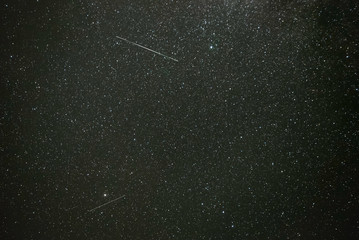 USA, Nevada, Nye County, West Stone Cabin Valley. Iridium satellite flares with visible glint pass across a dark night sky with dense stars.