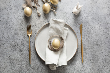Elegant easter table setting with golden eggs and bunny on grey. Top view.