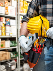 Electrician in the electrical parts store holds the level in hand, helmet with protective goggles....