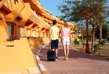 Young couple standing at hotel upon arrival, looking for room, holding suitcases