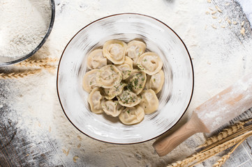 Russian traditional pelmeni with meat on a white plate. Wheat spikes, on a wooden board