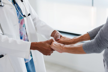 Hands of a doctor holding hands of elderly patient. Checking symptoms of stroke. Medical care and support concept.