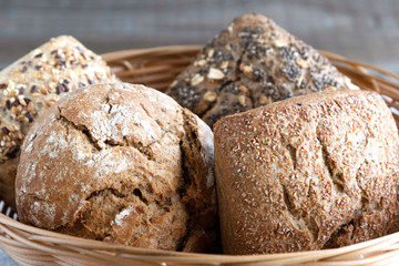 Four different buns with seeds lie in a wicker basket for bread. Close-up. Fresh baked goods in a bakery.