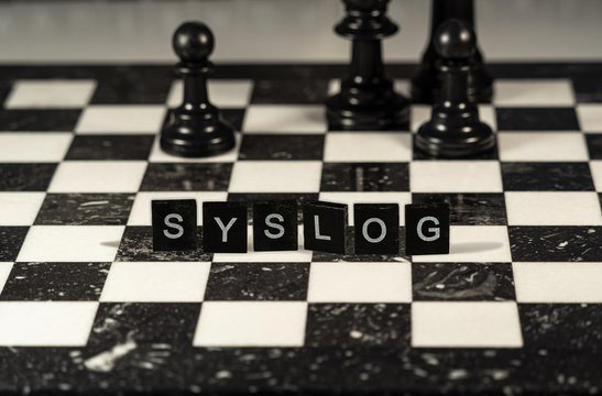 The concept of Syslog for system log represented by black and white letter tiles on a marble chessboard with chess pieces