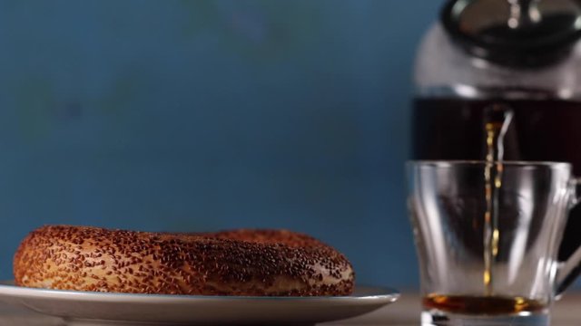 Pouring turkish tea into the cup with teapot and turkish simit is at background