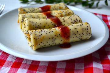Traditional Russian and Ukrainian this pancakes with poppy seeds and strawberry jam on a white plate. National food for Maslenitsa.