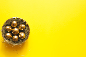 The golden eggs in a basket with straw  nest on a yellow background with a view from above.A background for celebrating Easter. Top view,Flatlay.