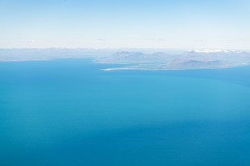 Keflavik, Iceland airport with aerial high angle view of Reykjavik city from airplane window above and colorful ocean water