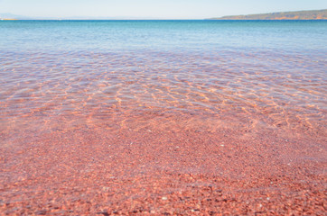 Vibrant red pebbles against blue water from low angle on a sunny day