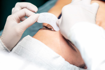 Cosmetologist's hands are putting the strip under the eye of young woman before the eyelash extension procedure, close up.