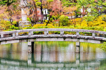 Naklejka premium Eikando temple stone bridge closeup in garden reflection in Kyoto, Japan during early spring with green and orange trees and buildings