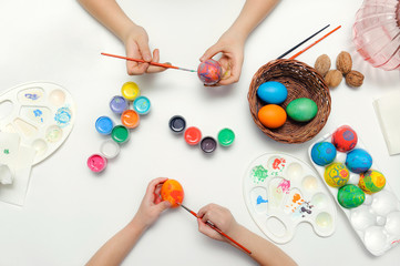 Joint traditional coloring of the symbol of Easter. Hands, brushes, paints, palette, eggs on a white background