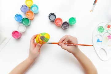 A child draws on the symbol of Easter. Children's hands on a white background paint a brush egg