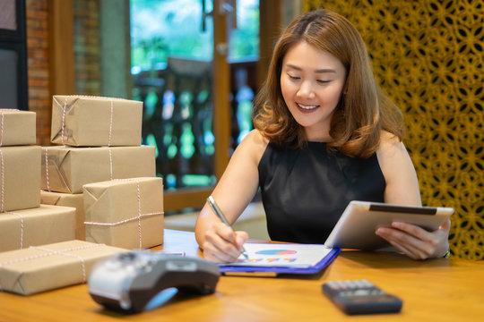 Asian woman using smartphone or digital tablets chatting and checking stock product in warehouse. checks the number of items boxes store delivery to customers, Asian owner or small business concept. - Powered by Adobe