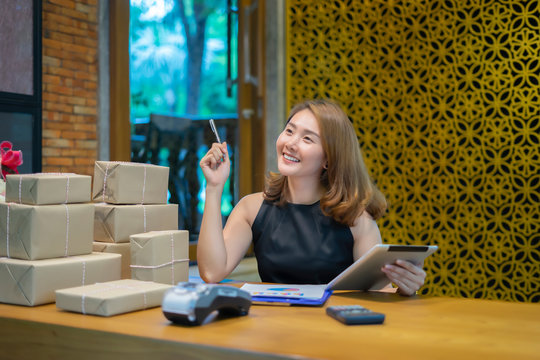 Asian woman using smartphone or digital tablets chatting and checking stock product in warehouse. checks the number of items boxes store delivery to customers, Asian owner or small business concept.