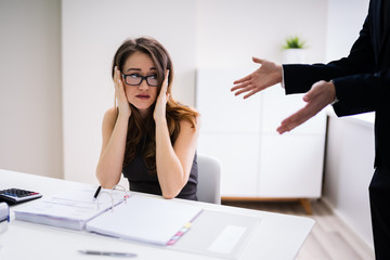 Boss Shouting At Employee Sitting At Desk