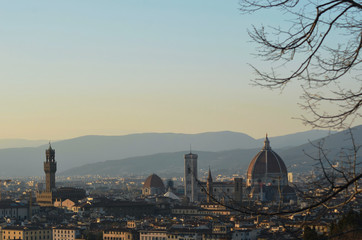 Fototapeta na wymiar The bare branches of a tree frame the view over the city of Florence, Italy at dusk. The Duomo, Baptistery and Campanile dominate the skyline. Hills are in the background. The sky is clear.