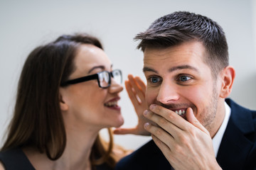 Businesswoman Whispering Into Male Partner's Ear
