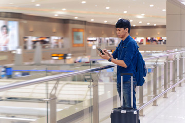 travel vacation concept.Asian man in airport or train station using travel app on a smartphone call someone,Asia male tourist reading map while waiting for taxi or bus with a bag, ready for journey