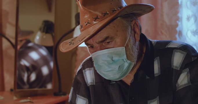 Portrait Of Ill Senior Man In Hat And Medical Mask Looks At Camera With Sadness