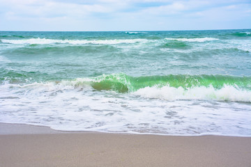Fototapeta na wymiar waves crash on sandy beach. cloudy weather before storm on the sea