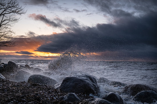 A fan of spray wave on a sunset, strewn with boulders shore of the Gulf of Finland.