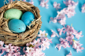 Easter background with blue Easter eggs in nest of spring flowers. Top view with copy space. Happy Easter Spring Festive greeting card. Holidays arrangement.