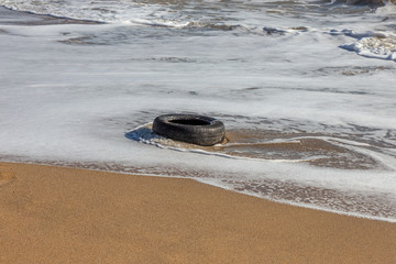 Old car tires on the beach,Water and sea coast pollution car tires on sand beach,An image of an old car tire ingrown into the sand.Old car tires with seaweed stuck on.