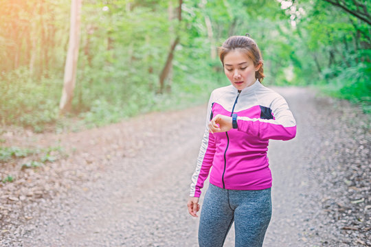 Asian Woman setting up the fitness smart watch for running. Sportswoman checking watch device,Forrest mountain road, exercise workout in nature road Autumn city forest park in fitness Sports concept