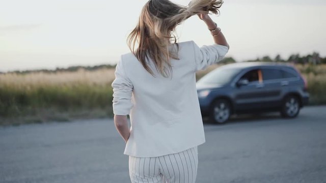 Lady in white suit corrects her hair and walking to the car out of city