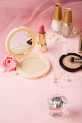 Woman's cosmetics on romantic pink lacy tulle background. Women's morning secrets. Cosmetics, lipstick,perfume, brush, powder, highlighter, concealer,patelle with eye shadows. Female cosmetics.Make up