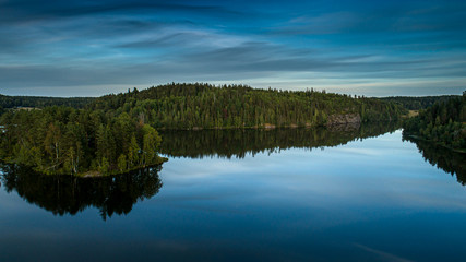 Reflection of the blue sky and green forest in the calm water of the lake.