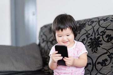 IT education, elementary preschool, learning, technology for people life concept,2 years old child having fun using a smartphone,little Asian girl with a mobile phone at home.asia baby plays indoors