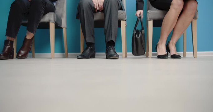 Group of three people in formal clothing sitting on chairs in queue line and waiting for their turn on job interview. New candidates worrying during expectation. Close up.