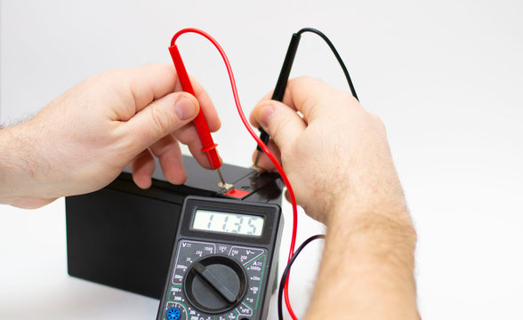 An electrician checks the voltage on the battery with a multimeter.