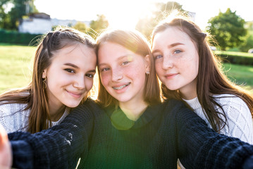 3 girls schoolgirls, selfie photo on phone camera, rest after school weekend. Summer in city, portraits close-up. Emotions of happiness, fun, joy, laughter, smile. Best girl friends. Freckles braces.