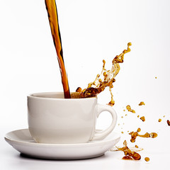 Coffee pouring into a white cup isolated against a plain white background, splashing in all directions creating a mess