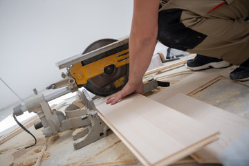 Man cutting laminate floor plank with electrical circular saw