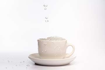 High speed studio photograph of water pouring and splashing into a white mug, isolated against a plain white background