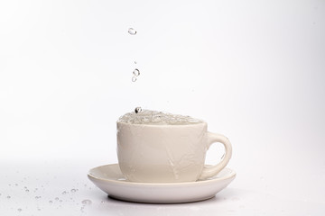 High speed studio photograph of water pouring and splashing into a white mug, isolated against a plain white background