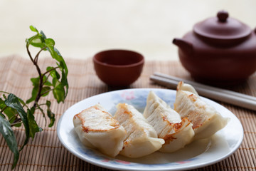 Close up of potstickers on plate with chopsticks, teapot and tea cup in background. A Chinese style potsticker mean being served.