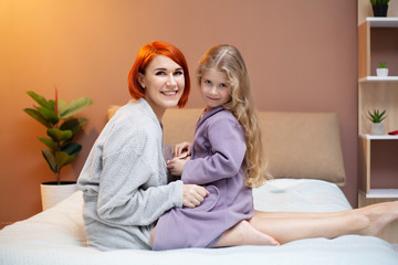 Happy mother and her baby daughter girl on bed in bedroom.