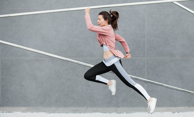 Fototapeta premium An athletic young woman is jumping, doing acrobatics, ballet, is actively involved in sports, against a concrete wall.