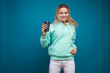 Happy girl smiling and drinking coffee, portrait in Studio on blue background.