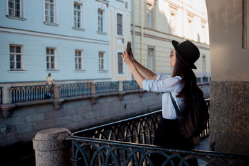 Tourist in the city takes a photo on smartphone. A young woman in a black hat and a white shirt,